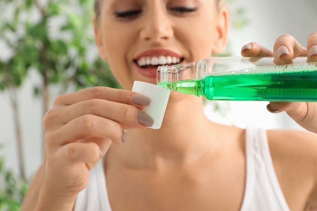 picture of a woman smiling while purring a green mouthwash