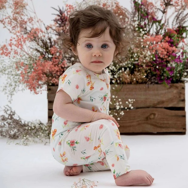 picture of a baby in onesies sitting on the ground beside flowers
