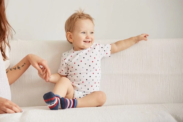 picture of a baby sitting on a soffa wearing bodysuit for newborn and socks 
