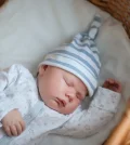 picture of a baby sleeping in a crib wearing baodysuit for newborn and a hat