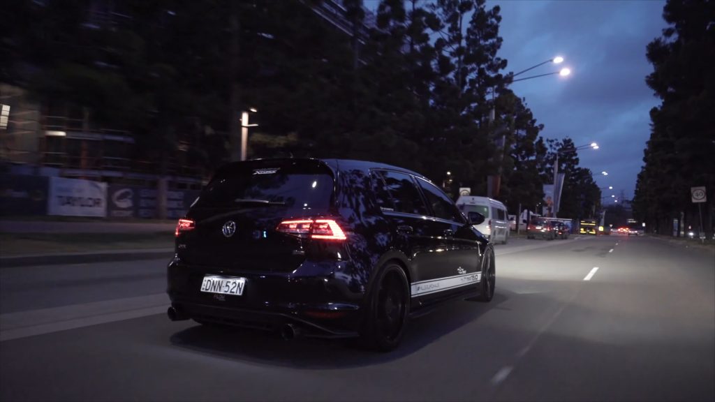 Night scene with Volkswagen Golf GTI featuring XFORCE branding, driving on a city street, showcasing aftermarket exhaust.