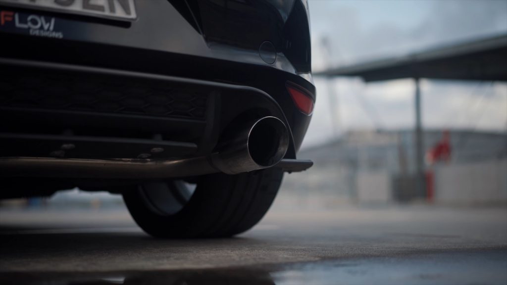 Understated single exit performance exhaust pipe on a black hatchback car, captured at ground level with a blurred background.