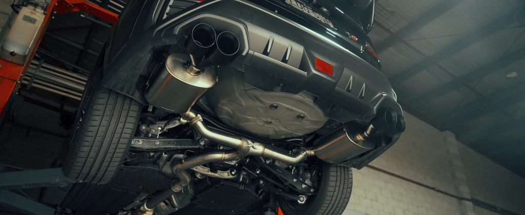 Close-up of dual exhaust pipes on a high-performance car with an intricate metal exhaust system underneath.