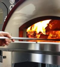 man putting pizza in the wooden pizza oven