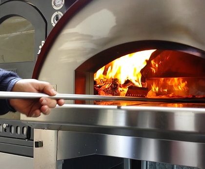 man putting pizza in the wooden pizza oven