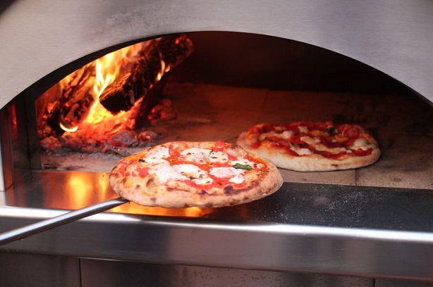 man putting two pizzas to bake in the wood pizza oven